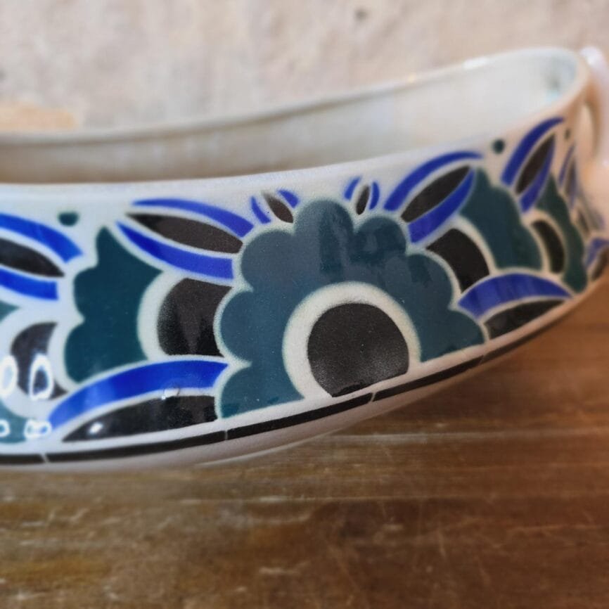 Zoom sur le motif floral stylisé de la jardinière ancienne, tons bleus et feuillage vert.