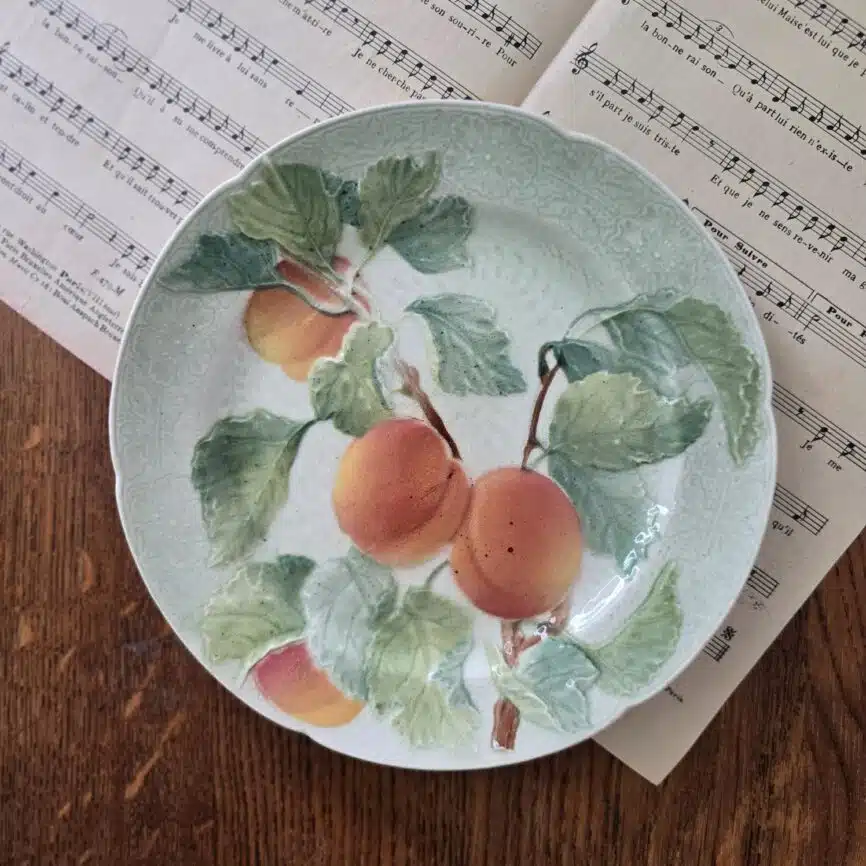 Assiette barbotine St Clément avec abricots et feuilles sur fond vert, présentée sur table bois avec document ancien