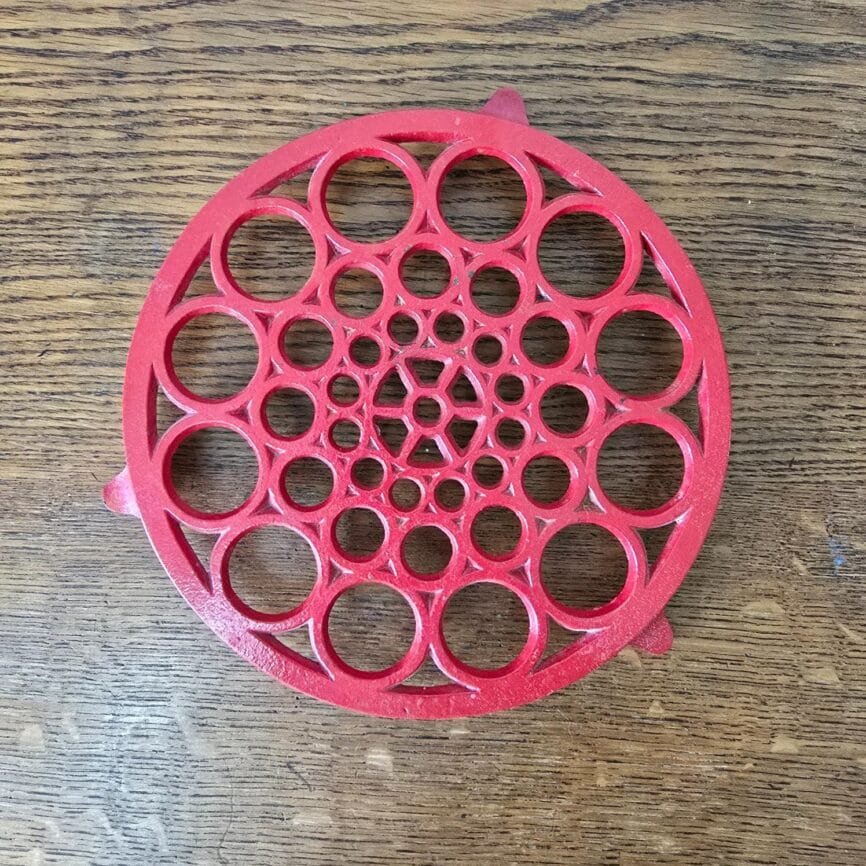 Dessous de plat vintage en fonte émaillée rouge, vue de dessus avec motif ajouré en bulles – objet déco cuisine rétro