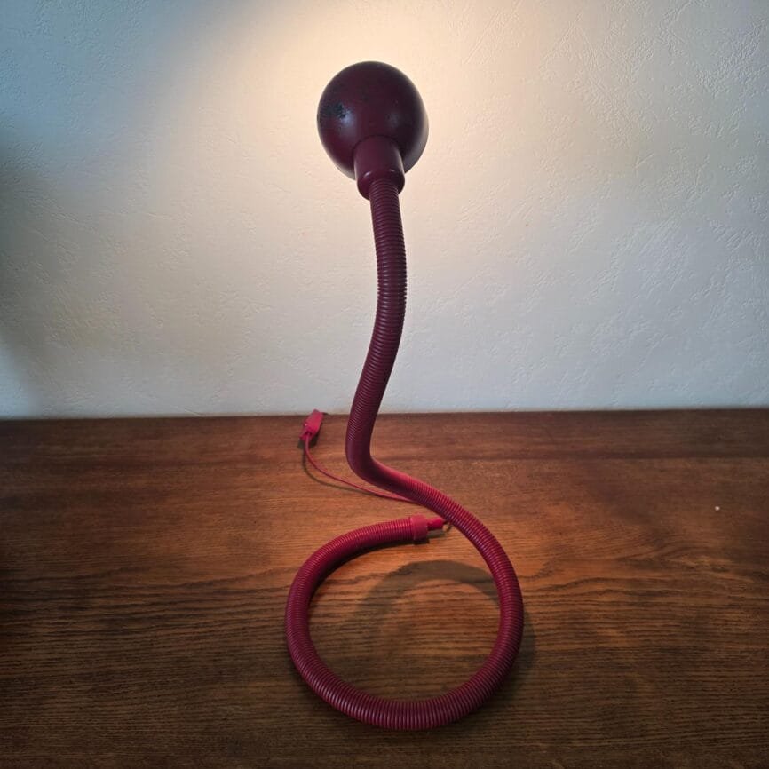 Lampe rouge allumée en vue de côté, lumière chaude dirigée vers le mur.