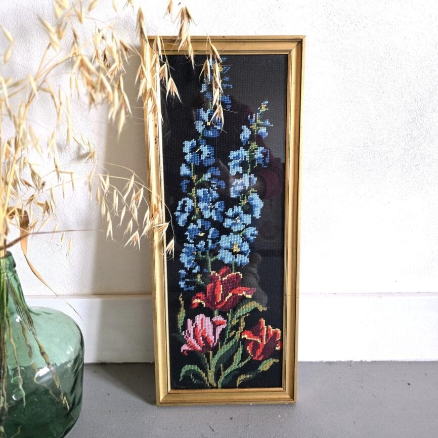 Cadre vintage doré avec canevas brodé de fleurs bleues et rouges sur fond noir – vue décorative