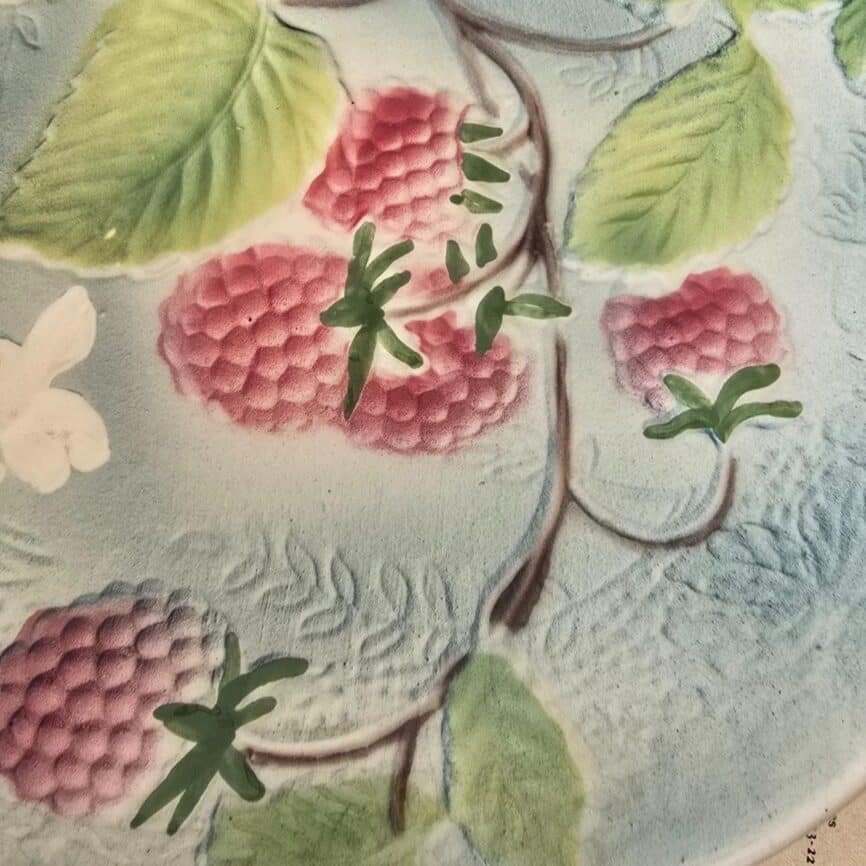 Zoom sur le décor coloré en barbotine avec framboises et feuillage.