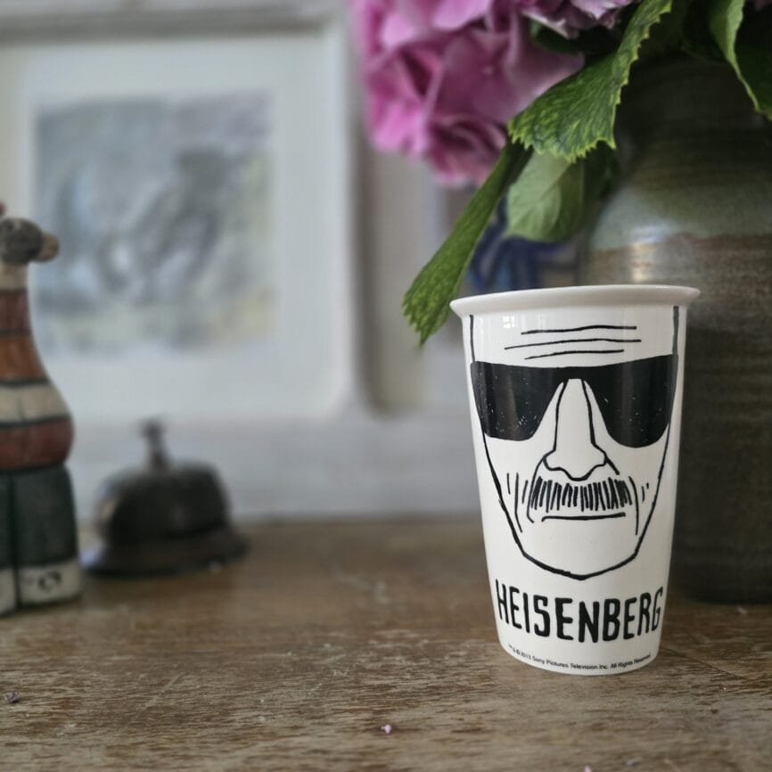Mug Heisenberg présenté debout sur une table en bois avec une fleur en arrière-plan.