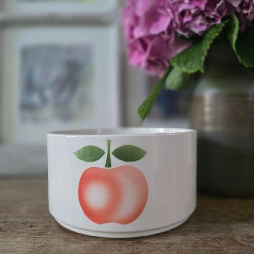 Saladier blanc en faïence Moulin des Loups décoré d’une pomme rose et verte, présenté sur une table en bois devant un vase d’hortensias.