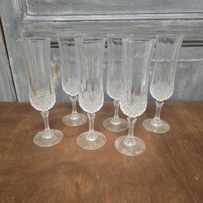 Lot de 6 flûtes à champagne vintage en verre transparent, décor ciselé, posées sur table bois.