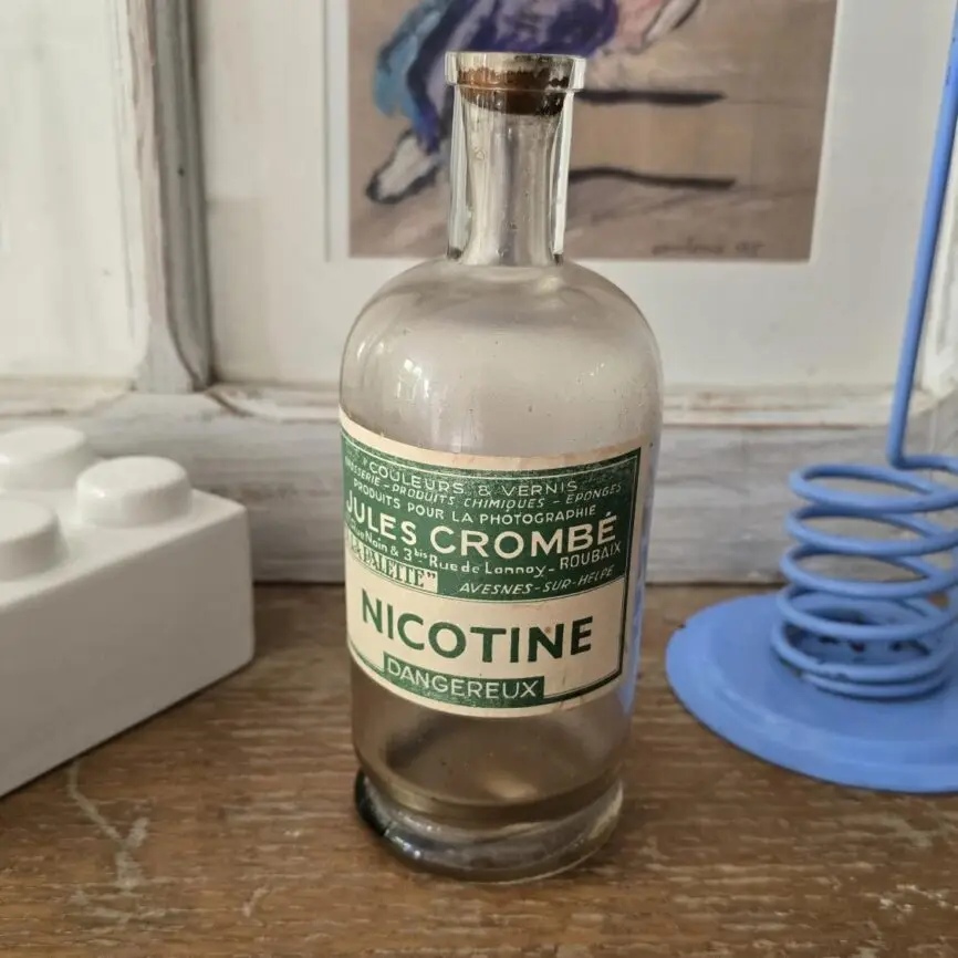 Ancienne bouteille de nicotine Jules Crombé, étiquette verte et blanche, vue de face dans un décor stylisé