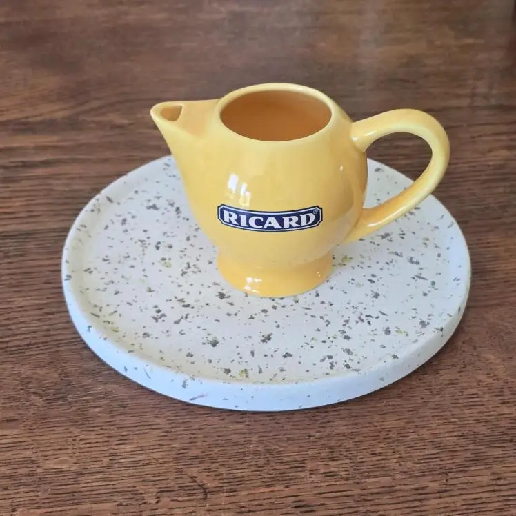 Petit pichet Ricard jaune en céramique, logo bleu, vu de face sur plateau décoratif.