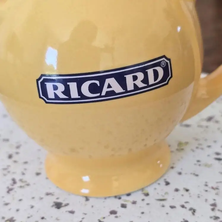 Gros plan du pichet Ricard jaune, anse et bec verseur arrondi.