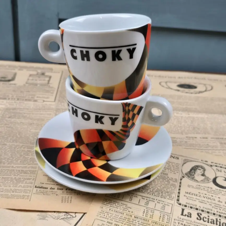 Lot de 2 tasses Choky vintage avec sous-tasses assorties, posé sur fond de journaux anciens.