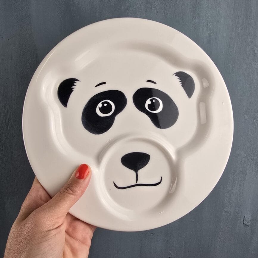 Assiette Panda tenue à la main, vue d’ensemble sur fond gris.