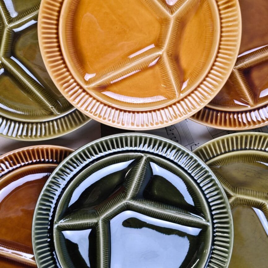 Vue rapprochée des six assiettes à fondue Sarreguemines dépareillées dans des tons verts et miel sur fond de bois.