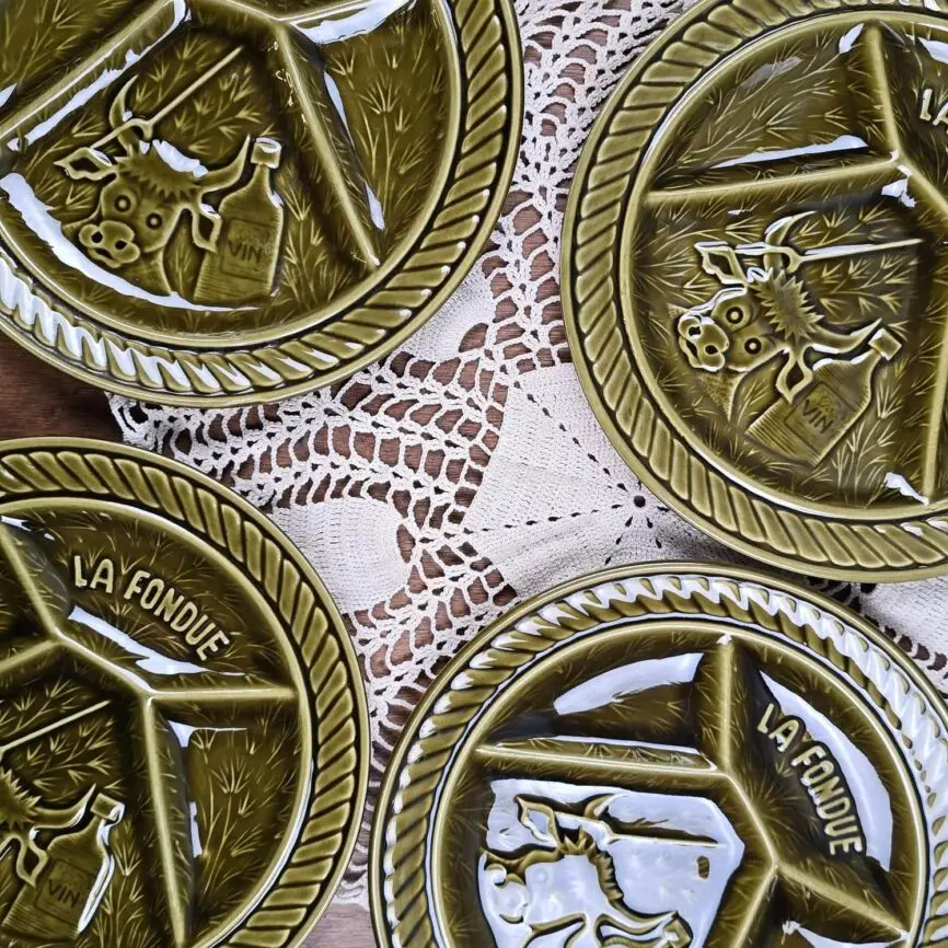 Détail du décor en relief des assiettes à fondue Sarreguemines, motif vache et inscription La Fondue, émail vert olive brillant.