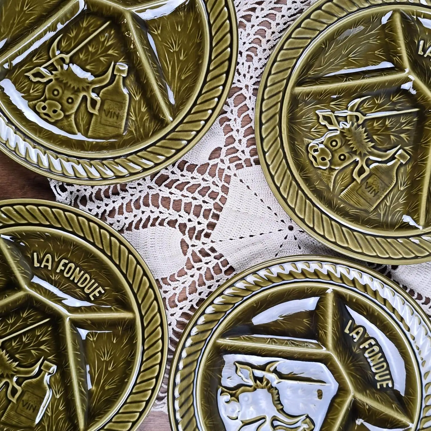 Détail du décor en relief des assiettes à fondue Sarreguemines, motif vache et inscription La Fondue, émail vert olive brillant.