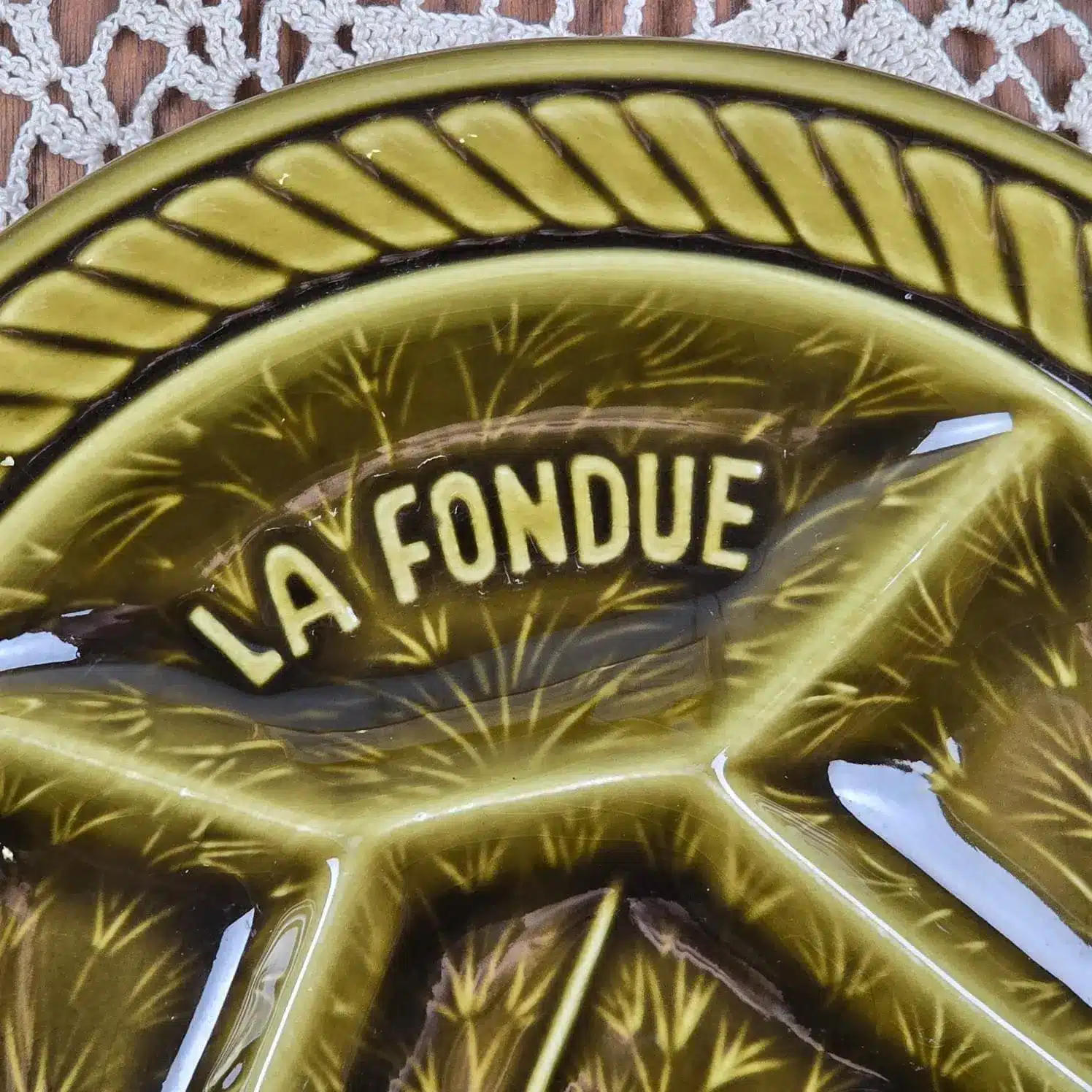 Détail du relief et de l’inscription La Fondue sur faïence Sarreguemines, émail vert foncé brillant.