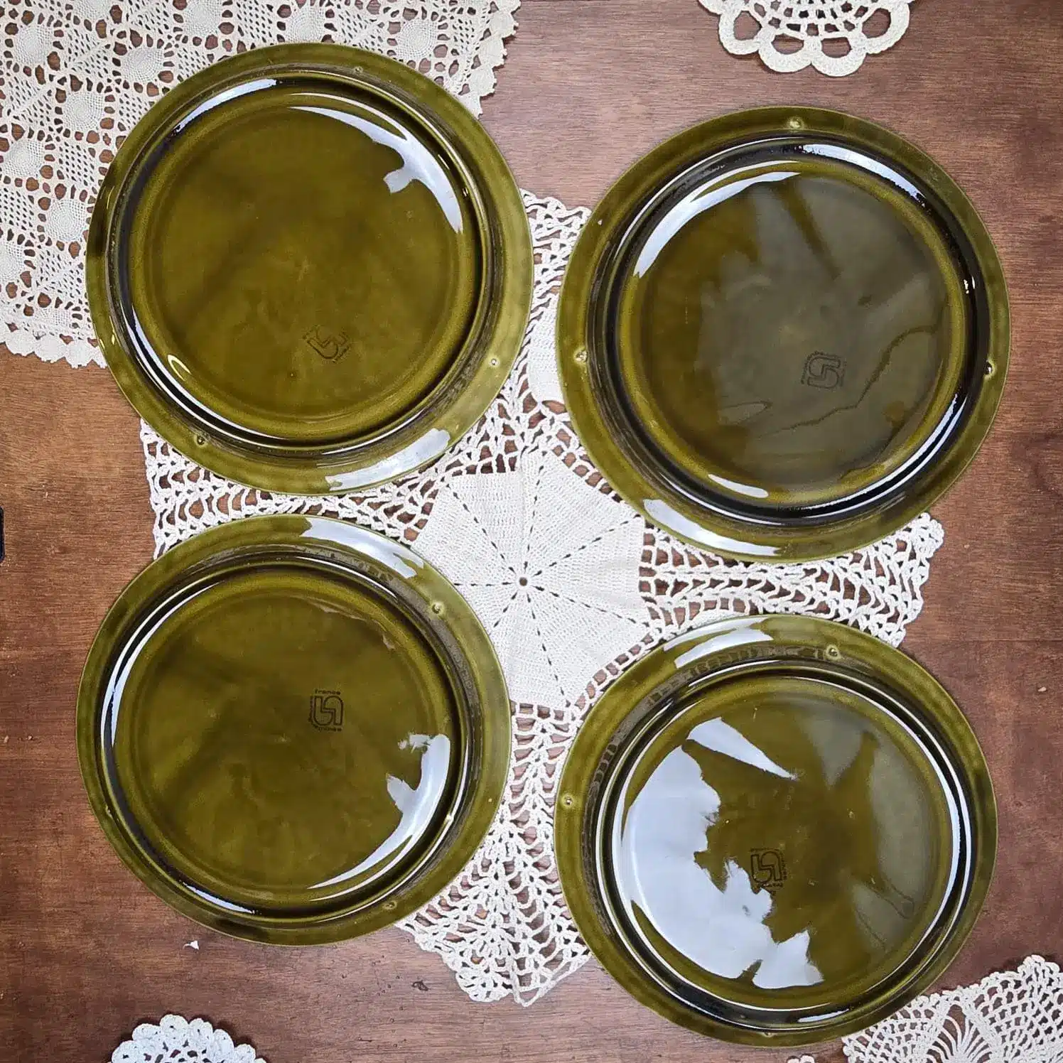 Vue d’ensemble des quatre assiettes à fondue Sarreguemines vertes, décor vache et bouteille de vin, vue de dos.