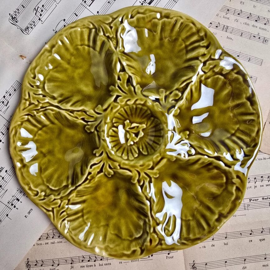Vue rapprochée d’une assiette Gien en barbotine vert olive, six compartiments en relief et émail brillant.