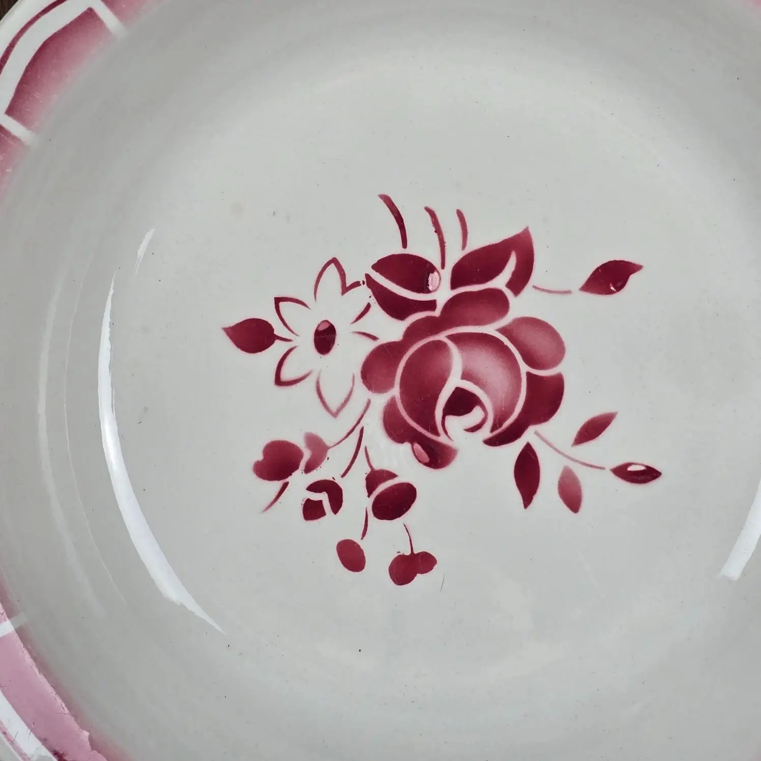 Gros plan sur le motif floral rose du plat Badonviller, avec une rose stylisée et des feuillages.