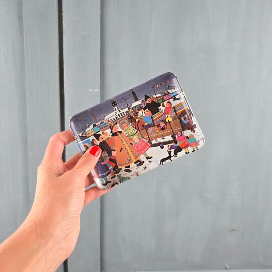 Plateau vintage Melel vu de face, tenu en main devant un fond gris, mettant en valeur la scène folklorique et les personnages colorés.