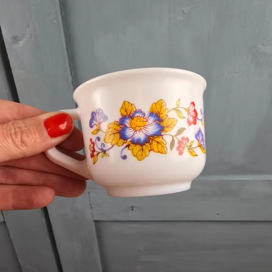 Gros plan sur une tasse Arcopal fleurie tenue en main, décor jaune bleu rouge