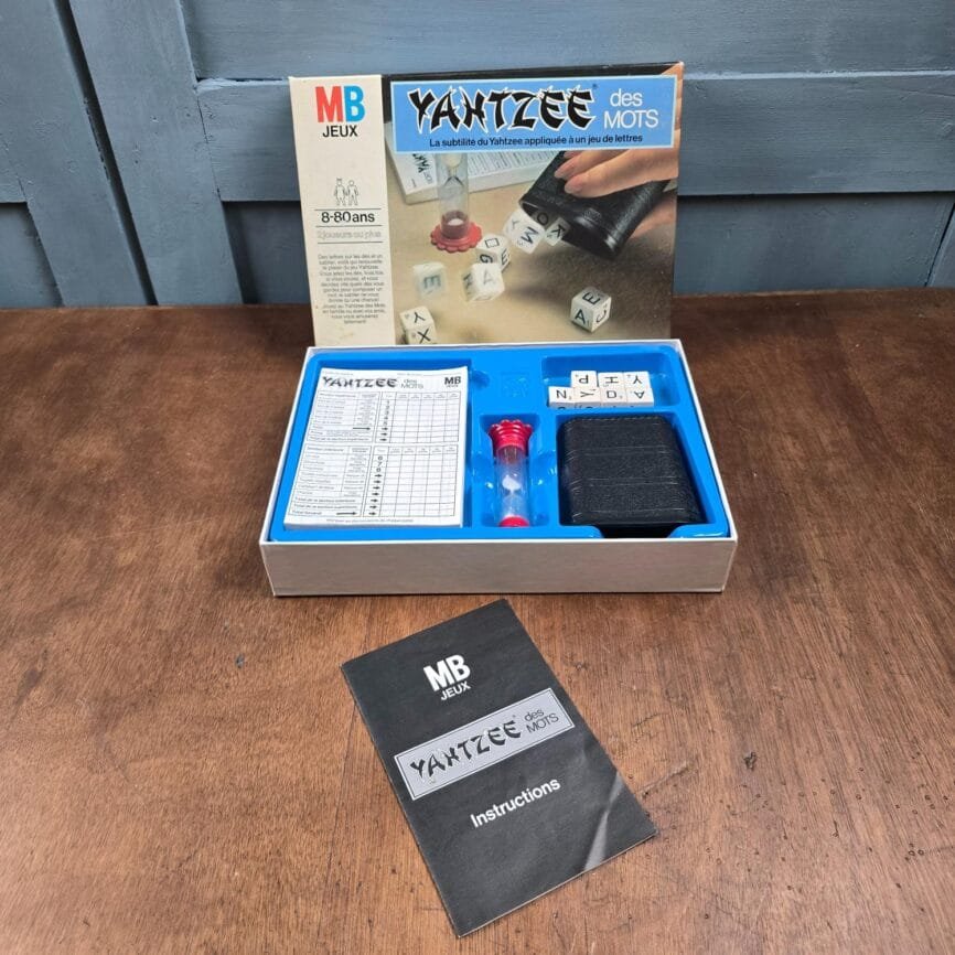 Vue d’ensemble du jeu Yahtzee des Mots : dés lettres, gobelet noir, sablier et bloc de feuilles de marque.