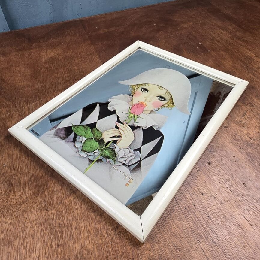 Miroir vintage Arlequin posé sur table, fond bleu et encadrement blanc.
