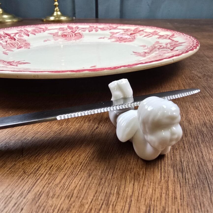 Repose-couteau ange en porcelaine blanche BB présenté sur une table en bois, avec un couteau posé dessus.