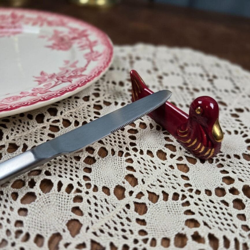 Repose-couteau vintage posé à côté d’un couvert sur napperon en dentelle.