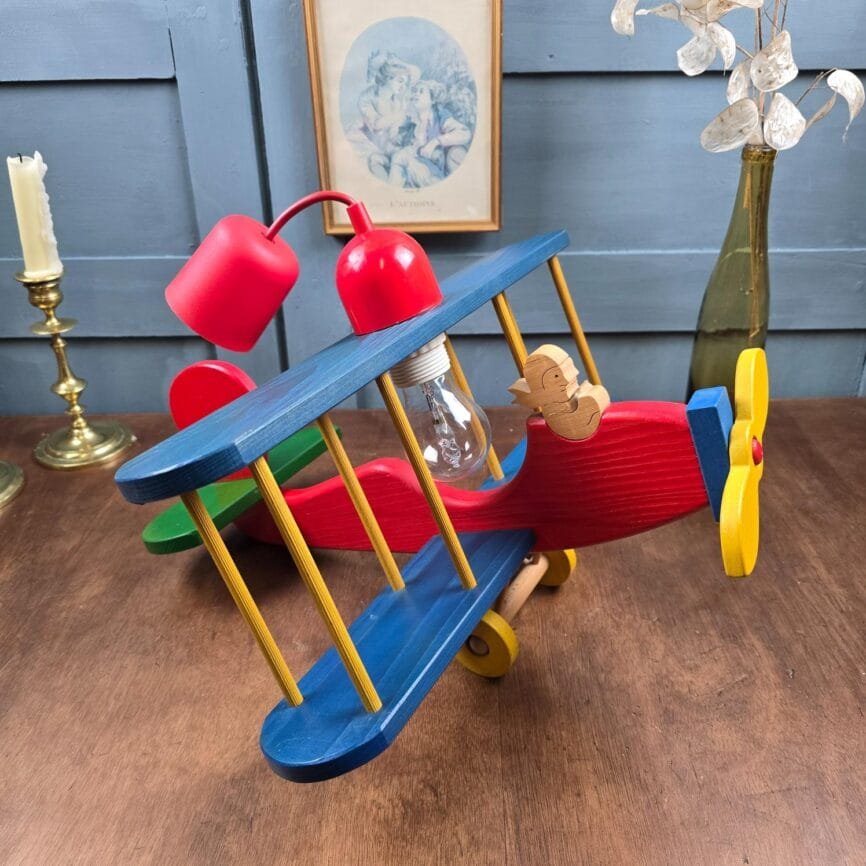 Vue d’ensemble de la suspension avion vintage en bois multicolore, modèle ESTO, posée sur une table en bois.