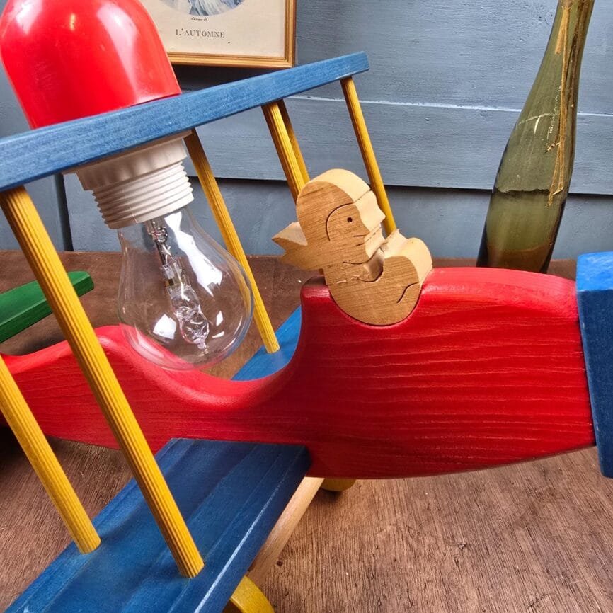 Détail du petit pilote sculpté en bois naturel sur le corps rouge de l’avion vintage.