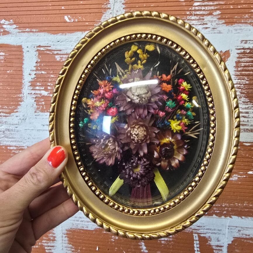 Vue de profil du cadre bombé ovale doré, soulignant le relief du verre et la profondeur de la composition florale.