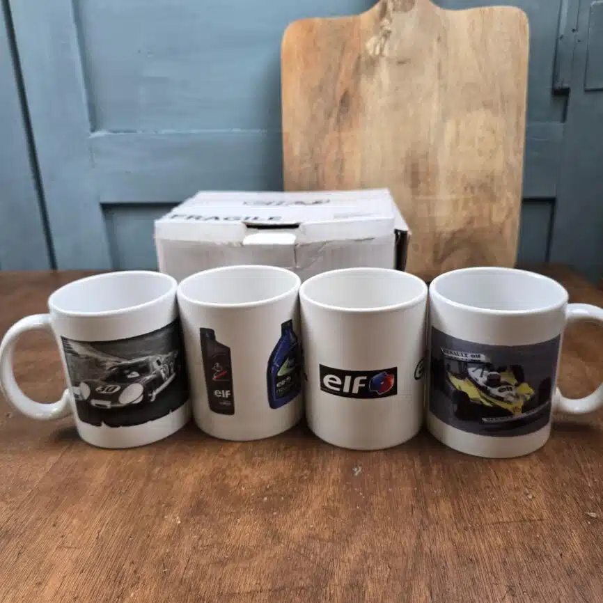 Ensemble de mugs ELF alignés devant la boîte d’origine, différents décors automobiles.