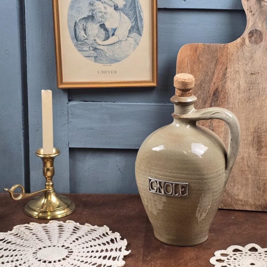 Bouteille ancienne en grès beige « Gnole » posée sur table en bois, ambiance vintage