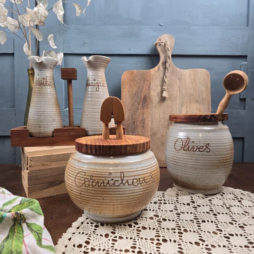 Ensemble Grès du Marais France en grès moucheté beige : huile, vinaigre, pot à cornichons et pot à olives sur table en bois.