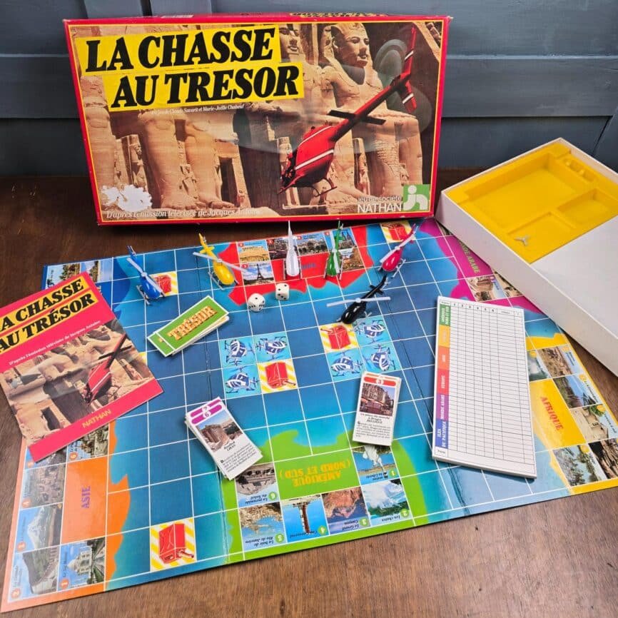 Jeu vintage La Chasse au Trésor Nathan, plateau, pions en forme d'hélicoptère, notice, cartes et dés posés sur table en bois