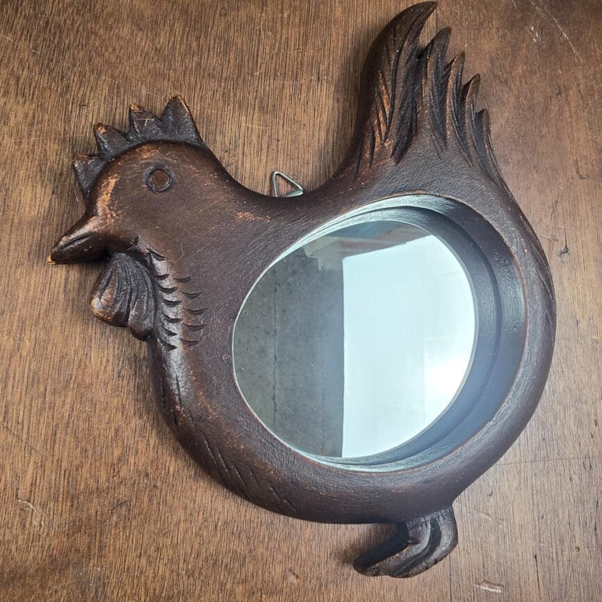Miroir mural vintage en bois sculpté en forme de poule posé sur une table en bois