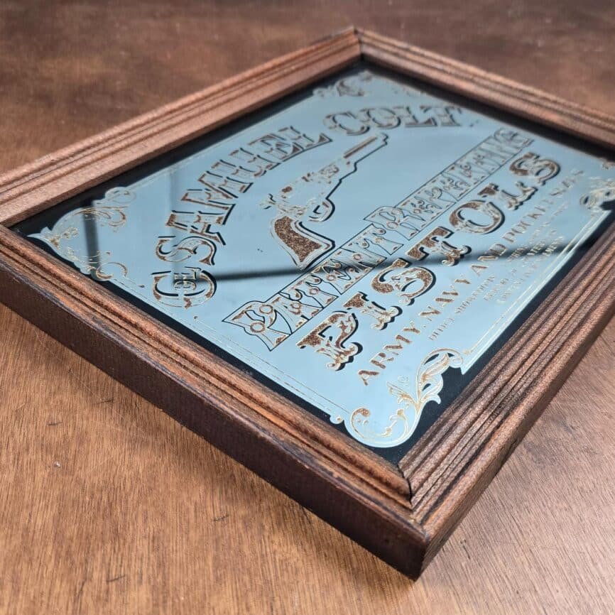 Miroir sérigraphié Samuel Colt vintage posé sur table en bois pour montrer l'épaisseur du cadre