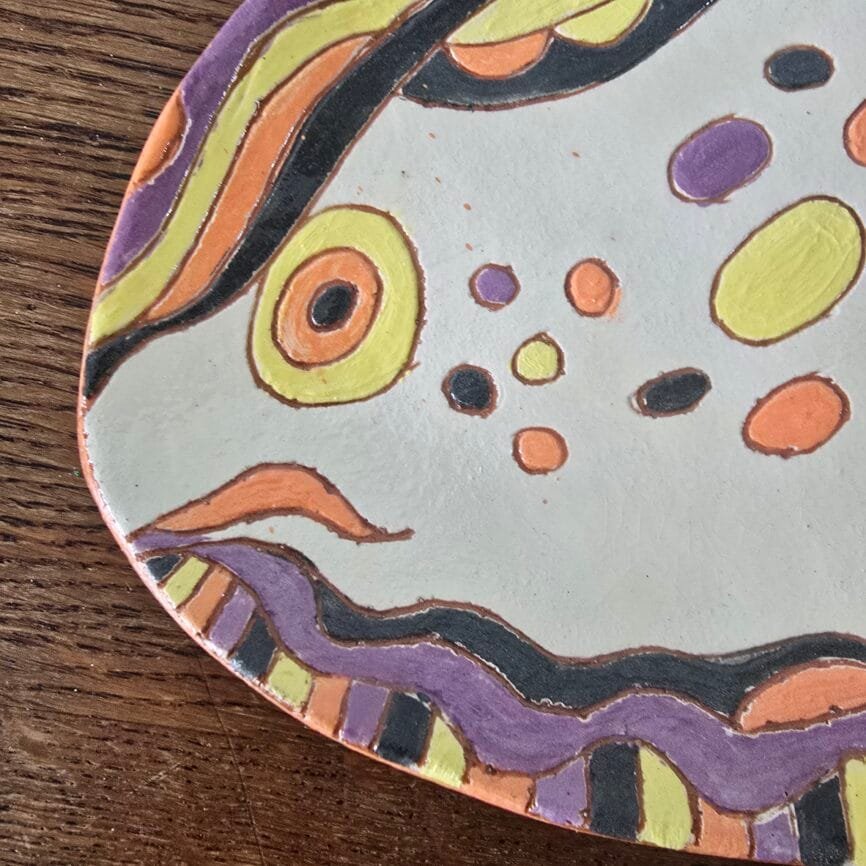 Assiette poisson artisanale peinte main en terre cuite colorée décor naïf, vue rapprochée sur la tête du poisson