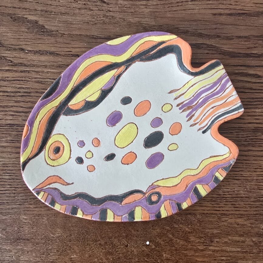 Assiette poisson artisanale peinte main en terre cuite colorée décor naïf, sur table en bois