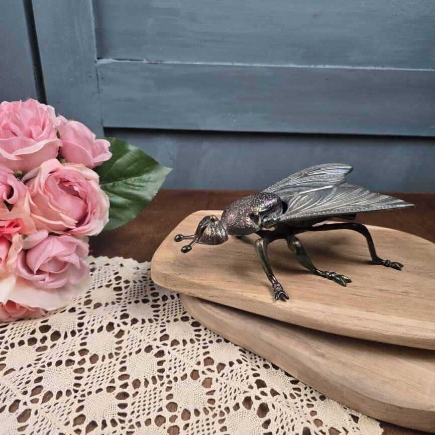 Mouche vintage ouvrante en métal irisé – Boîte décorative curiosité ou cendrier ambiance vintage sur table en bois et fleurs roses