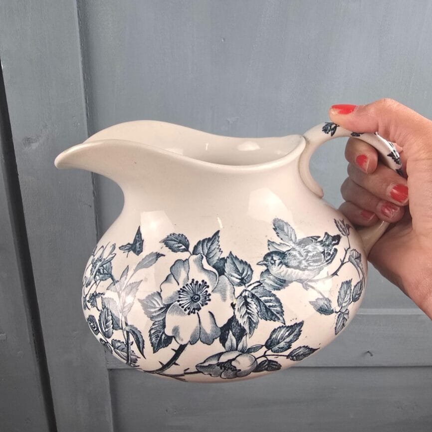 Broc à eau joufflu fleuri décor oiseaux bleus vintage, tenue en main sur le décor oiseau