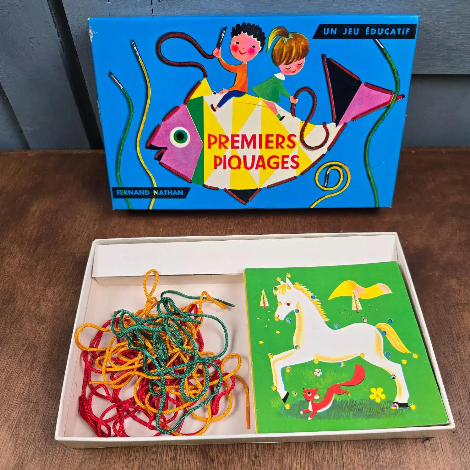 Jeu éducatif vintage Premiers Piquages Fernand Nathan sur table en bois, ouvert, montrant le contenu de la boîte