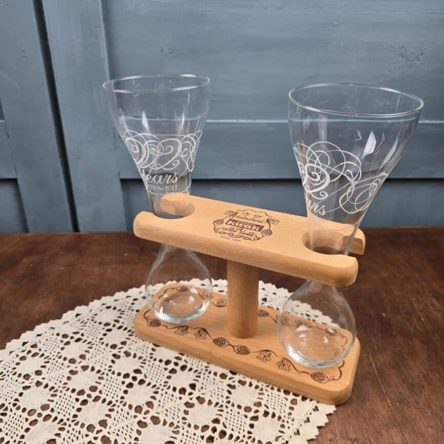 Set de 2 verres duo à bière Kwak édition limitée 222 Years avec support bois, posé sur table en bois et napperon