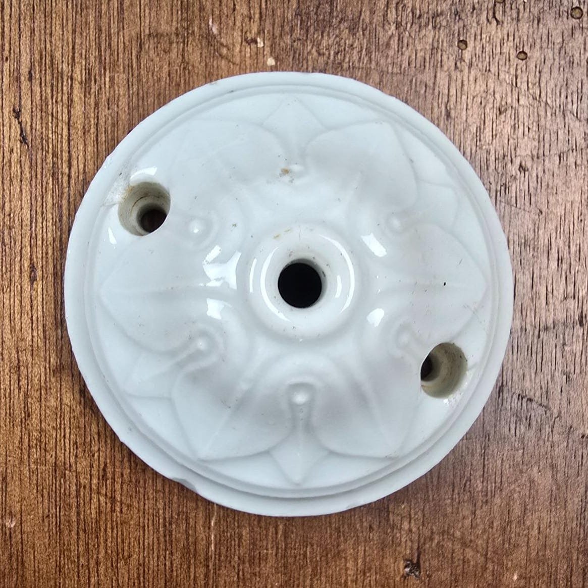 Rosace de plafond ancienne en porcelaine blanche vue de dessus sur table en bois