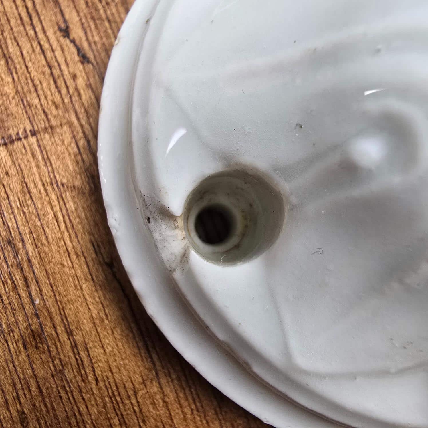 Rosace de plafond ancienne en porcelaine blanche, vue rapprochée de l'ébréchure au niveau de l'emplacement de la vis