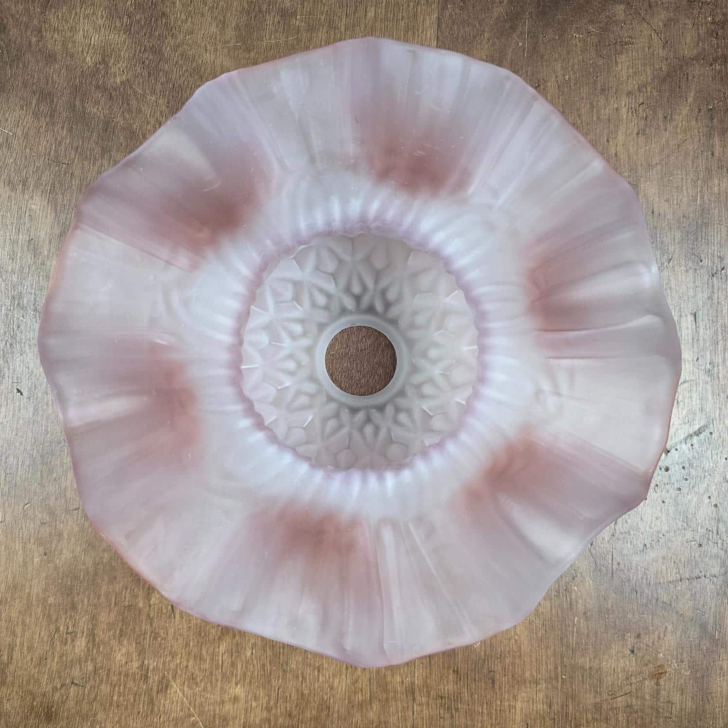 Abat-jour ancien en verre rose satiné, bord ondulé, vue de dessous sur table en bois