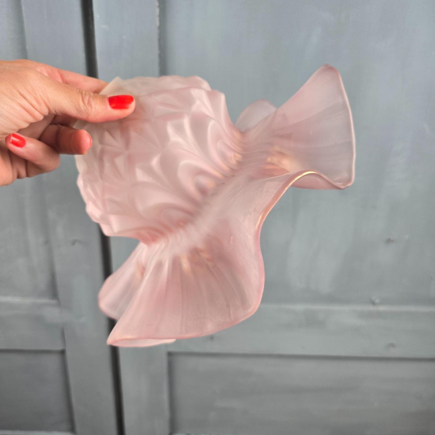 Abat-jour ancien en verre rose satiné tenu en main de profil pour montrer les bords ondulés