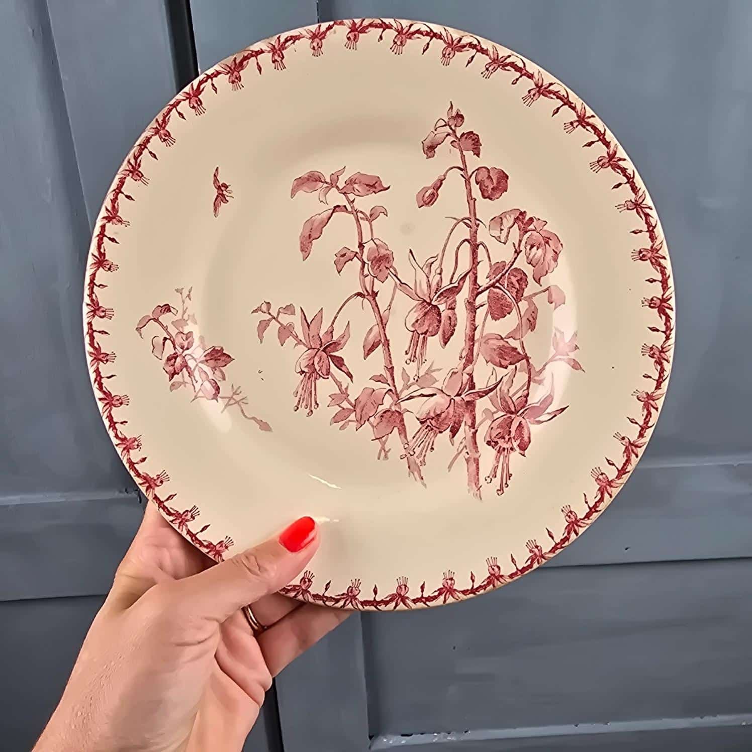 Assiette ancienne Gien Fuchsia en terre de fer tenue en main pour mettre en évidence la beauté de cette assiette