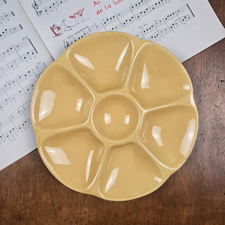 Assiette à huîtres Gien jaune ocre, présenté sur table en bois et sur partitions de musique