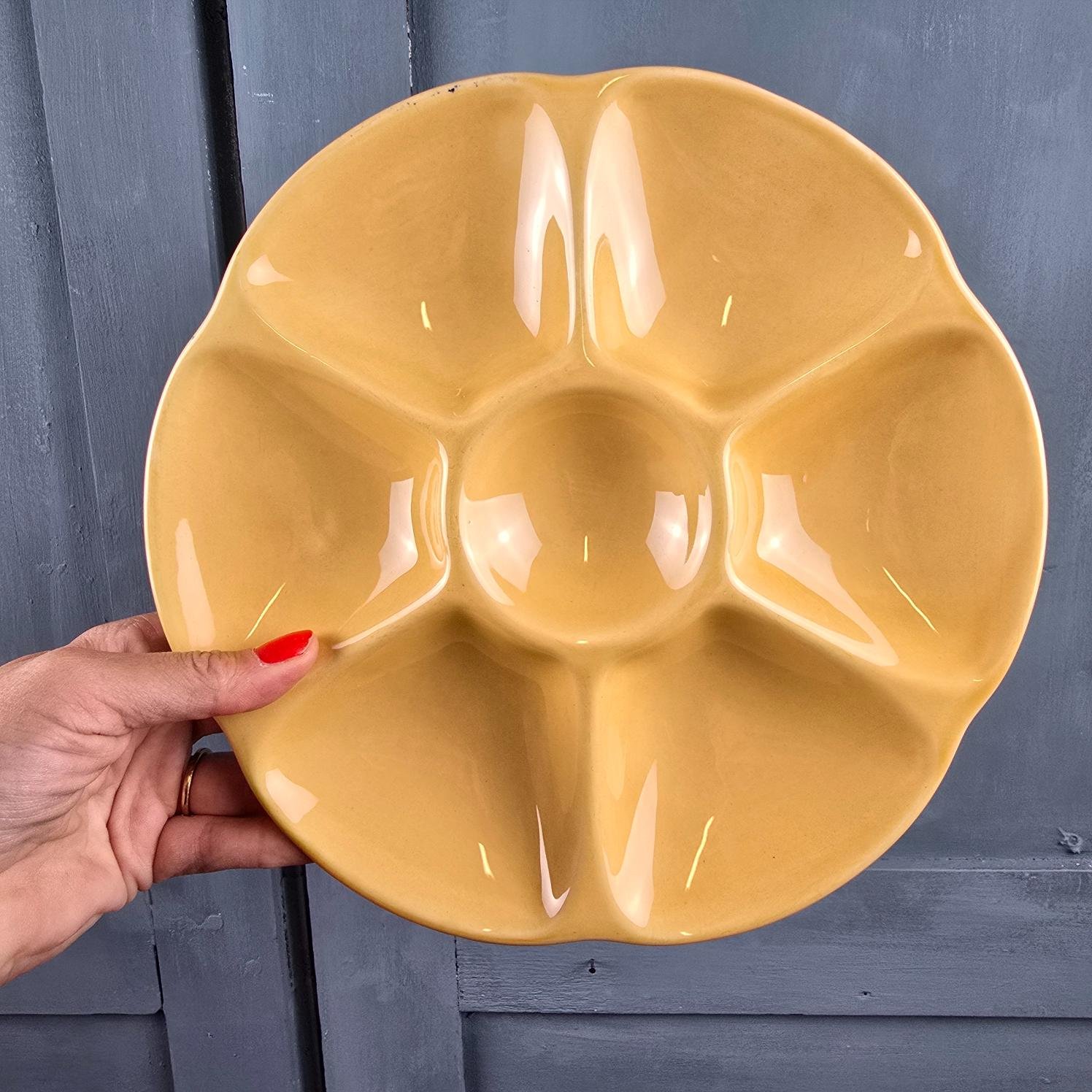 Assiette à huîtres Gien jaune ocre, tenue en main permettant d'imaginer le rendu accrochée mur