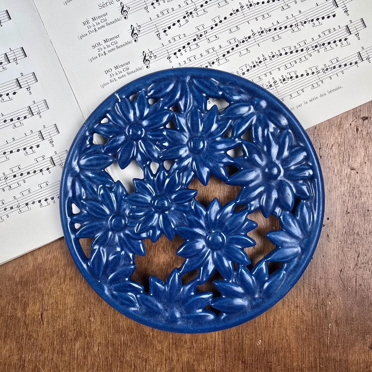 Dessous de plat en fonte émaillée bleue à fleurs Invicta, ambiance vintage sur partition de musique